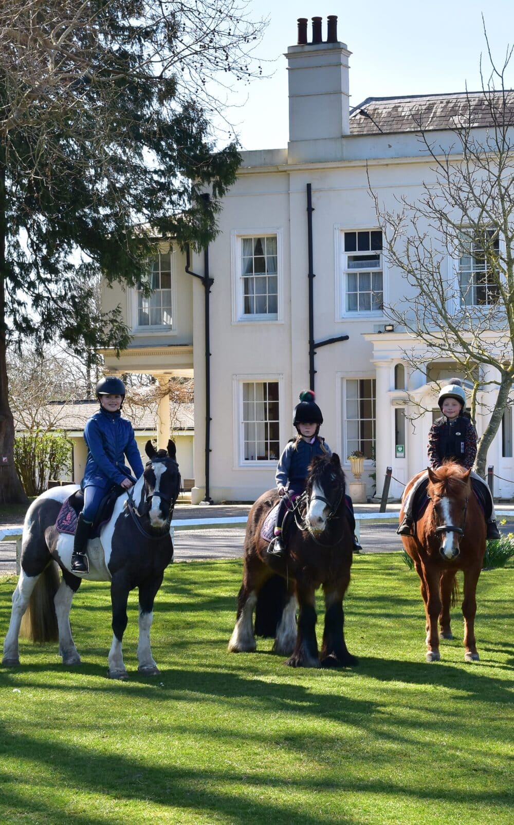 Three pupils on horses in front of prep school.